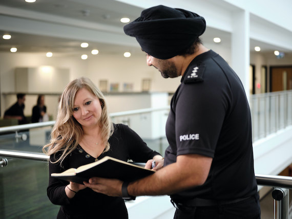 A police officer holding a book talks to a member of staff.