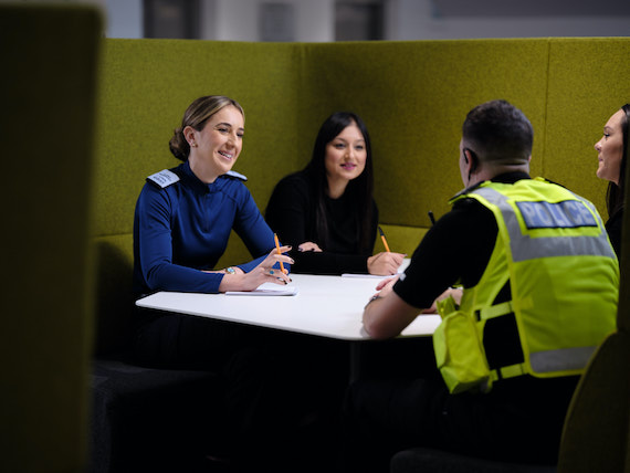 Two police officers and two staff members talk sat at a meeting table.